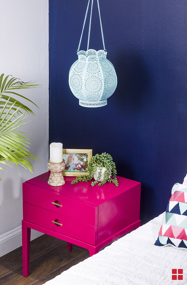 Bright pink nightstand under a turquoise light fixture.