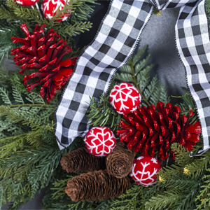 Close-up view of a ribbon, red berries and red and brown pine cones on a green wreath.