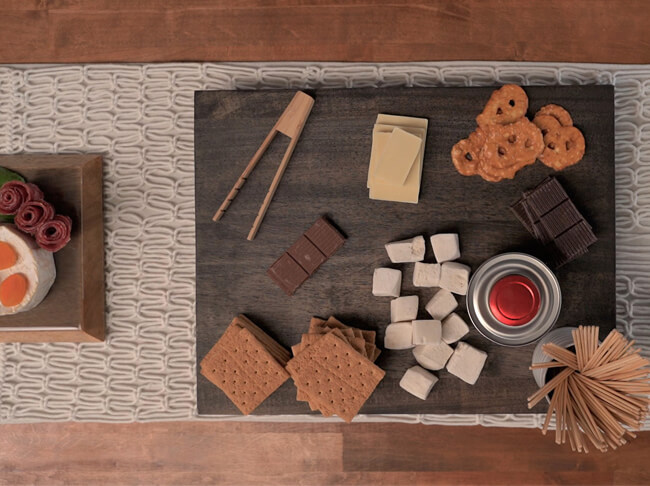 Crackers, cheese cubes and other snacks on a stained wood charcuterie board.