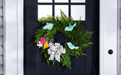 A green wreath with blue wooden birds and pink and yellow wooden flowers. 
