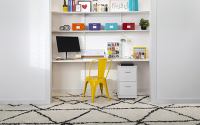 A closet office with shelves, a computer and a bright yellow chair.