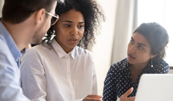 Three interns talking by computer.
