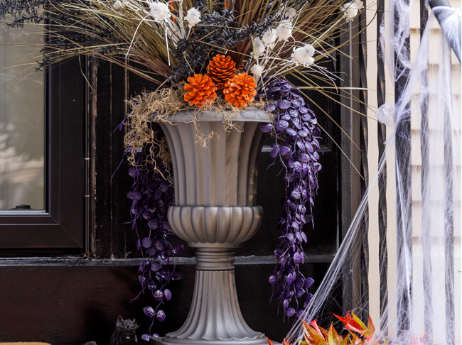 Spray painted urn filled with pinecones and branches painted black and orange.