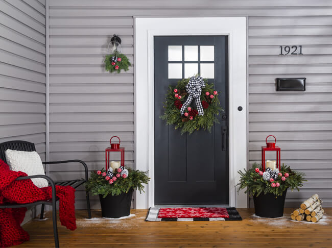 A front porch with a green wreath with red pine cones and a black and white bow hanging on a front door.
