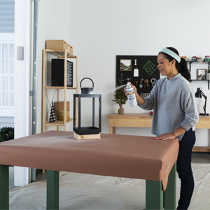 A woman applying white spray primer to a black decorative lantern.