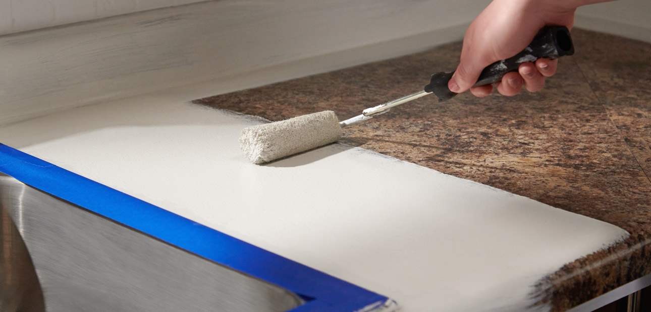 Using a roller to apply white basecoat to a brown countertop. 