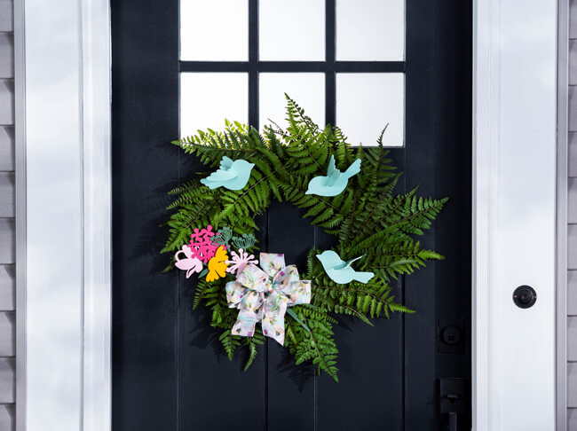 A green wreath with blue wooden birds and pink and yellow wooden flowers. 