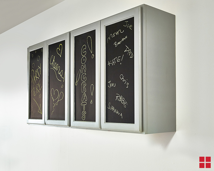 A white wall with a bank of light gray cabinets that have chalkboards on the doors.