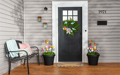Colorful wooden flowers and small birdhouses in two urn planters placed on either side of the front door. 