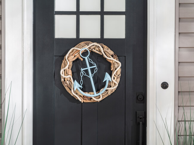 A wooden wreath with a light blue anchor in the center hanging on a front door.