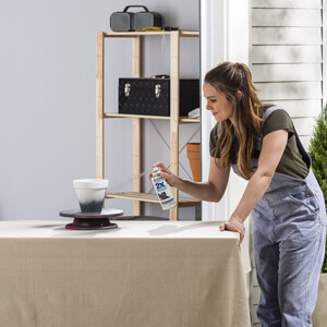 Woman spray painting white flower pot dark gray.