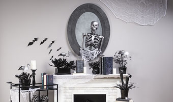 A fireplace mantel fireplace mantel decorated for Halloween below an oval mirror with a 3-D skeleton attached to the front. 